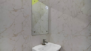 A bathroom with a white sink, a mirror, and marble-patterned walls. - Classic The Orchid Residency (Kolkata)