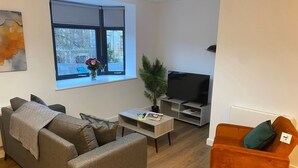 A living room with a sofa, a coffee table, a TV stand, and a plant. - Modern 2-Bed, Swindon Old Town (Swindon)