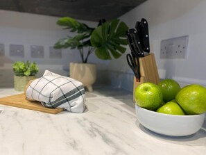 A kitchen counter with a bowl of green apples, a rolled-up cloth, and a knife block.