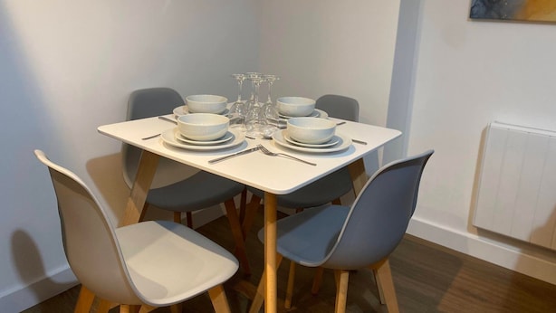 A dining table set with white plates, bowls, and wine glasses, surrounded by grey chairs. - Modern 2-Bed, Swindon Old Town (Swindon)