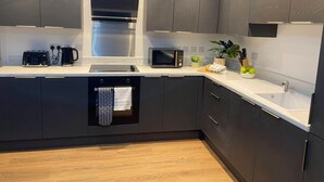 A modern kitchen with dark cabinetry, a stainless steel range hood, a built-in microwave, and a dishwasher. - Modern 2-Bed, Swindon Old Town (Swindon)