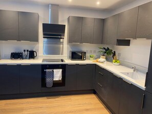 A modern kitchen with dark cabinetry, a stainless steel range hood, a built-in microwave, and a dishwasher. - Modern 2-Bed, Swindon Old Town (Swindon)