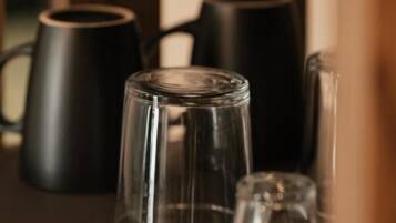 A shelf with several clear glass tumblers and black mugs.