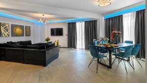 Un salon moderne avec un canapé noir, une table à manger avec des chaises et un téléviseur à écran plat fixé au mur.