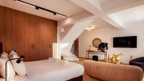 Une chambre moderne avec un grand lit, une table de chevet, un canapé, une télévision et un escalier menant à un niveau supérieur.