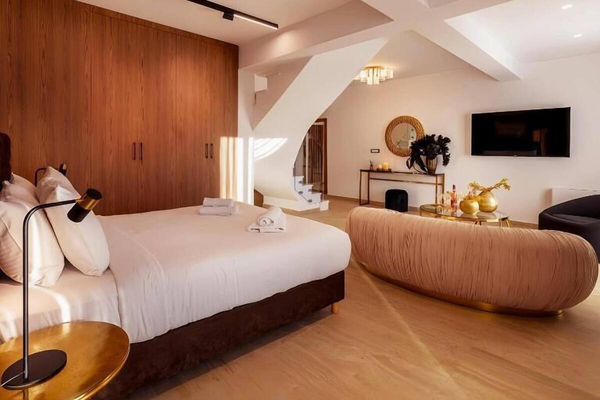 Een moderne slaapkamer met een groot bed, een nachtkastje, een bank, een televisie en een trap naar een hoger niveau.