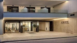 Un hôtel à plusieurs étages, doté d’un design moderne, avec une entrée imposante et une enseigne indiquant « CENS Luxury Suites ».