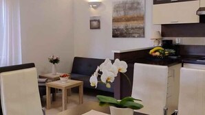 Ein modernes Wohnzimmer mit Essbereich, ausgestattet mit einer Couch, einem Couchtisch und einer Topfpflanze mit Orchideen.