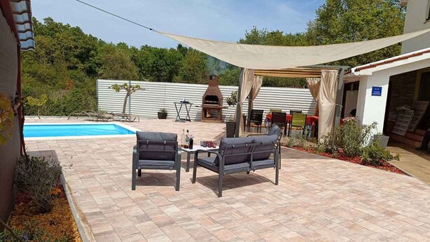 Een terras met een zwembad, zitplaatsen buiten en een barbecuehoek.
