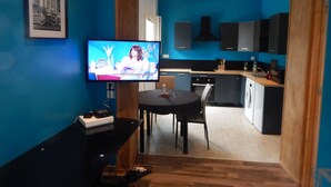 Een moderne woonkamer met een televisie, een eettafel en een keuken met kasten en een fornuis.