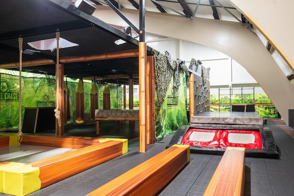 Un espace de jeux intérieur avec des bancs en bois, un trampoline et des murs décorés sur le thème de la jungle.