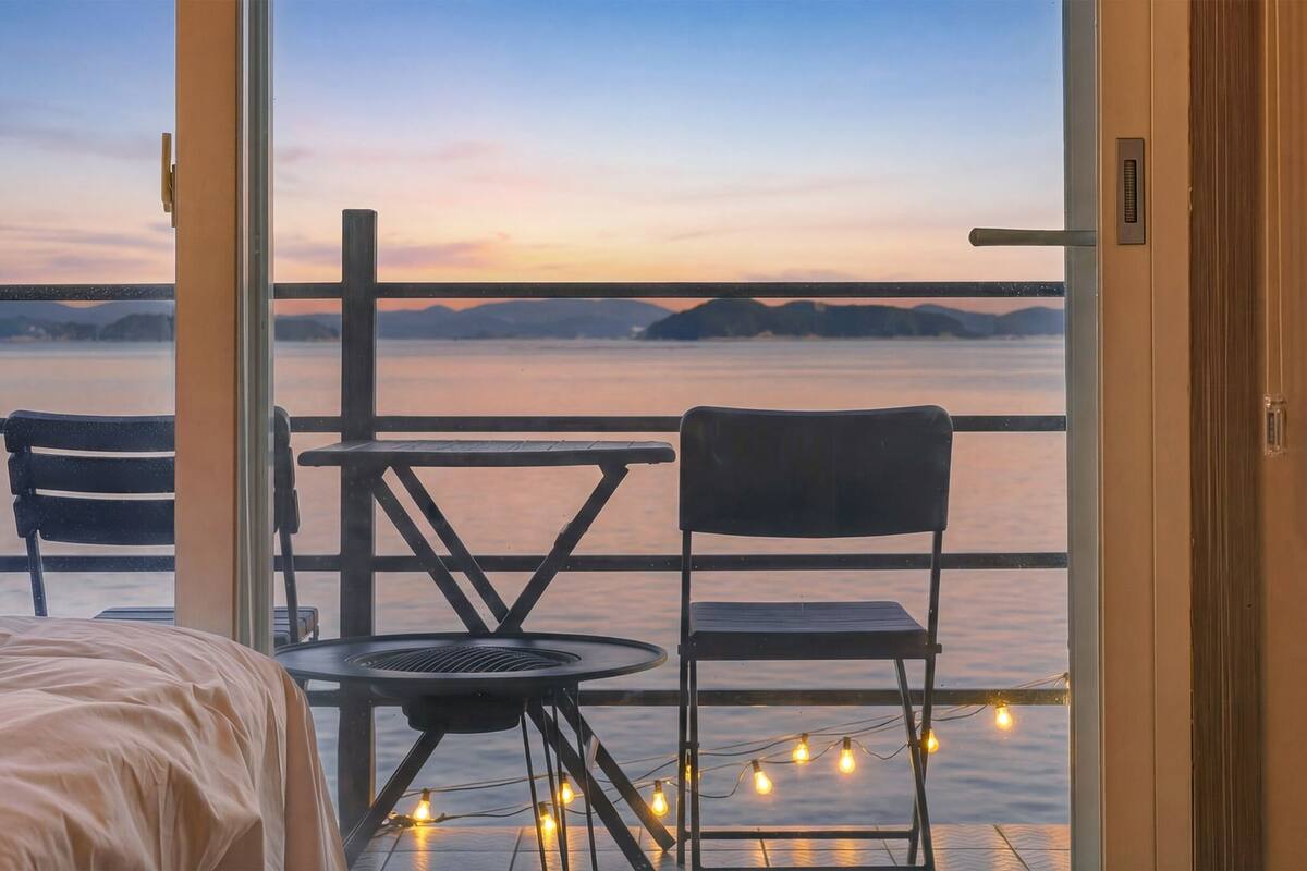 A balcony with two chairs and a small table, overlooking a body of water and distant land.