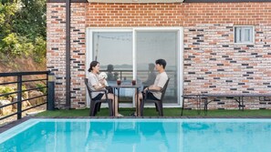 A poolside area with a brick wall, a glass door, and a small table with chairs. - Taean Solpleo Pool Villa (Taean)