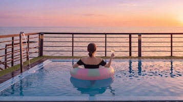 Una persona sentada en un flotador de piscina con vista al mar al atardecer.