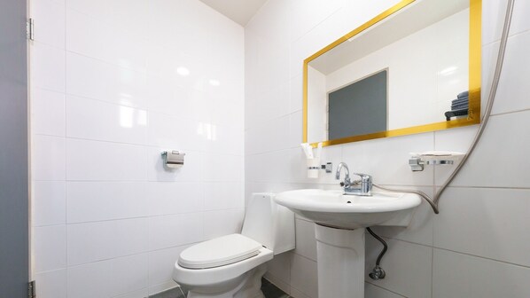 Un baño pequeño y moderno con azulejos blancos, un inodoro, un lavabo con espejo y un perchero para toallas.