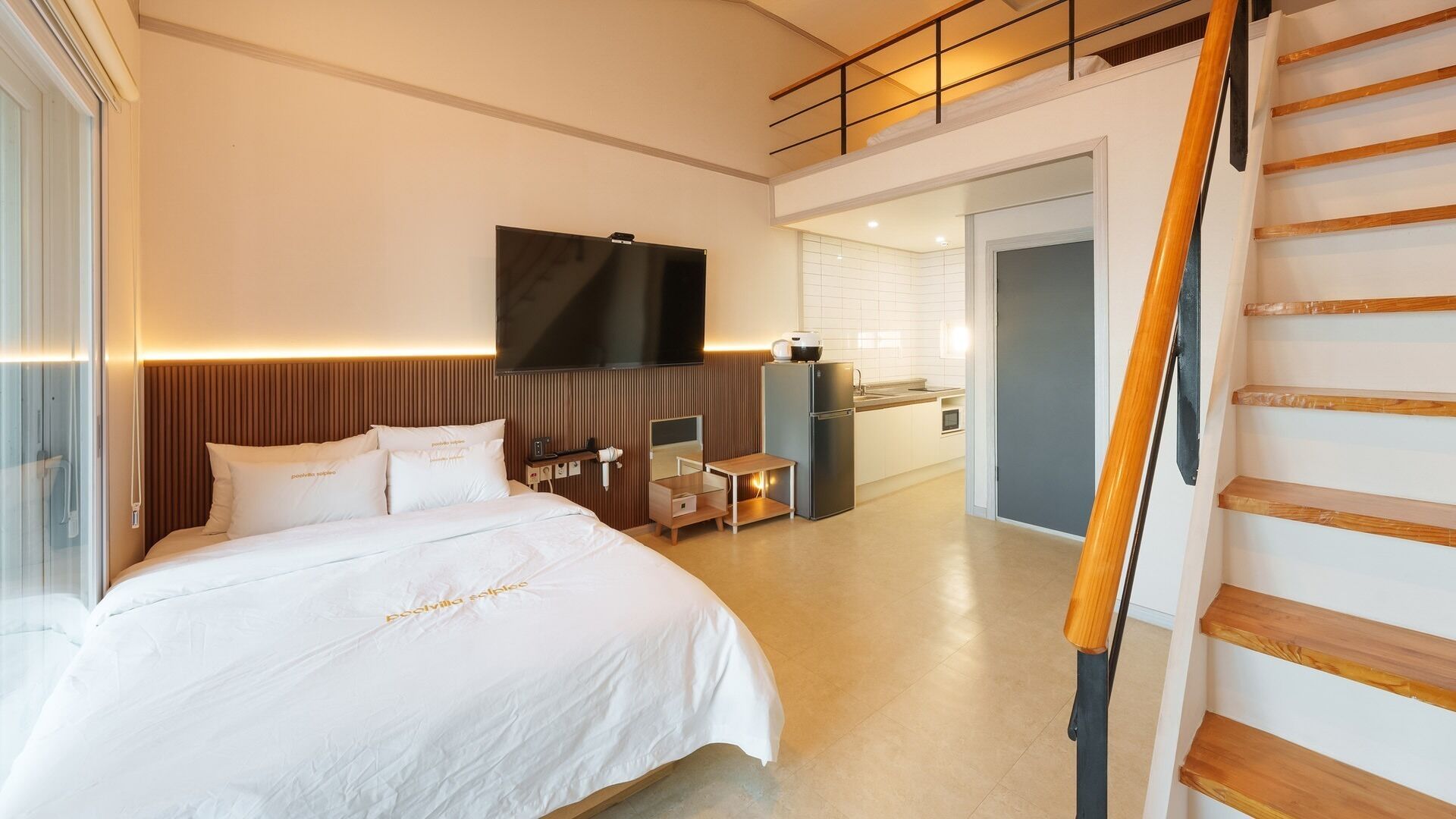 Una habitación de hotel moderna con una cama grande, un televisor de pantalla plana, un escritorio pequeño y una kitchenette.