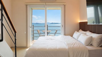 Habitación de hotel con cama, vista al mar y balcón con sillas.