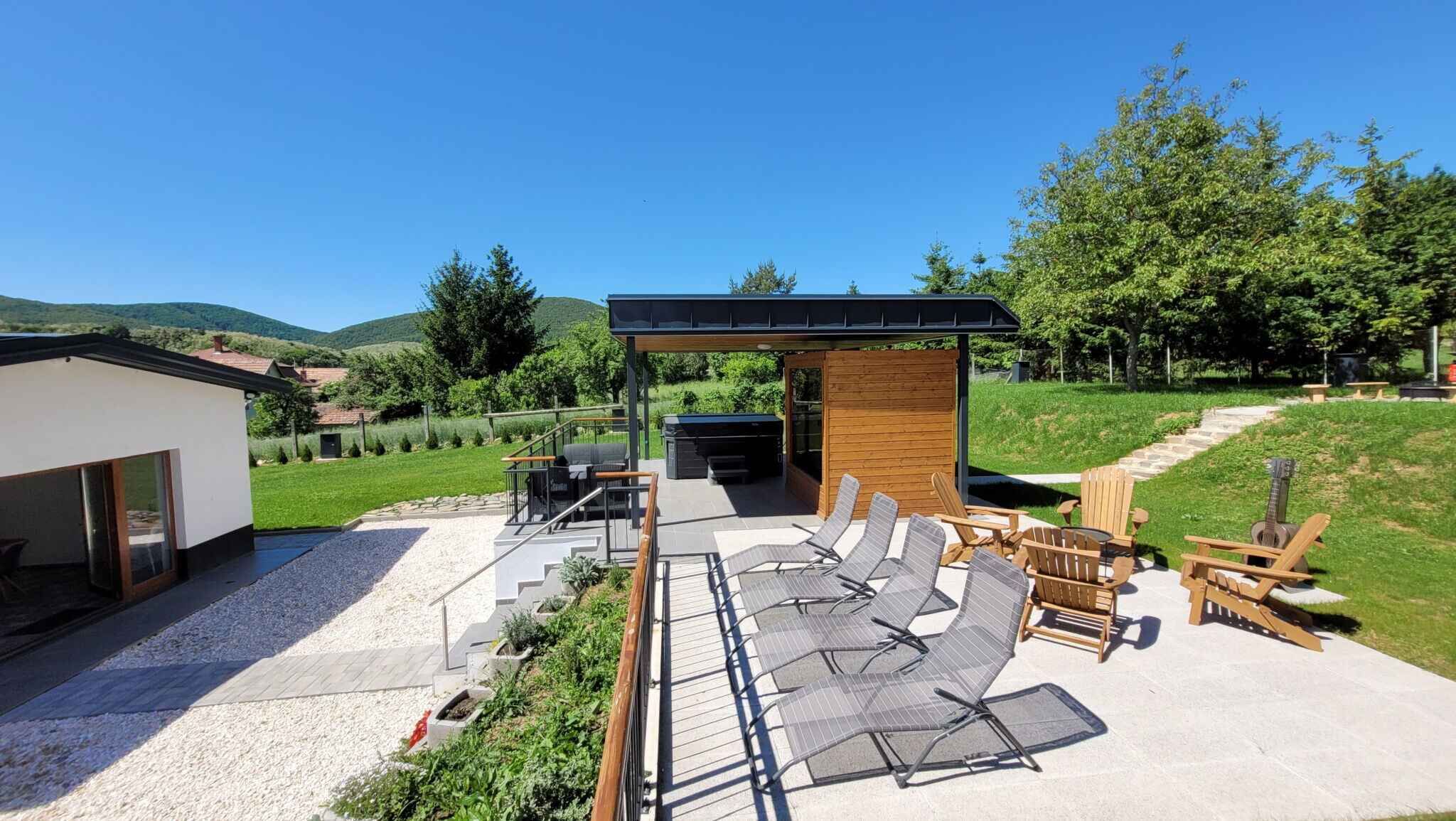 Un patio moderno al aire libre con sillones de sol, zona de barbacoa y un espacio de estar cubierto.