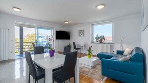 Uma sala moderna com área de jantar, um sofá azul e uma TV fixada na parede.