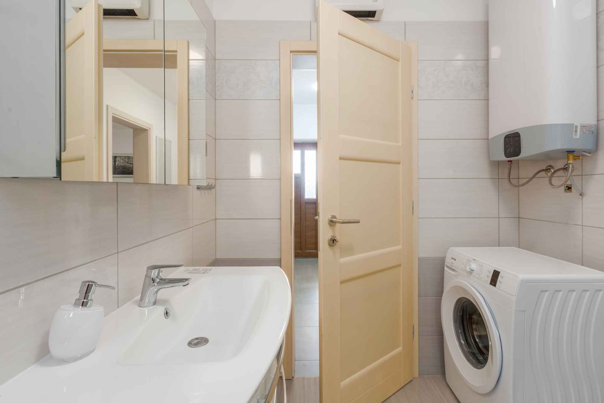 A modern bathroom with a sink, mirror, and a washing machine.