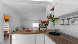 A modern kitchen with white cabinetry, a wooden countertop, and a black sink. There is a window with white blinds, a plant on the countertop, and kitchen utensils hanging on the wall. - Holiday apartment with air conditioning and balcony (Funtana)