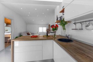 A modern kitchen with white cabinetry, a wooden countertop, and a black sink. There is a window with white blinds, a plant on the countertop, and kitchen utensils hanging on the wall. - Holiday apartment with air conditioning and balcony (Funtana)
