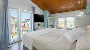 A bedroom with a large bed, wooden ceiling, sliding glass doors to a balcony, and a flat-screen TV mounted on the wall. - Holiday apartment with air conditioning and balcony (Funtana)