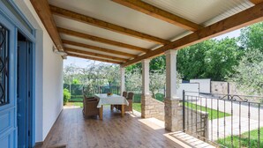 Eine überdachte Terrasse mit Holztisch und -stühlen, Steinpfeilern und einem Metallzaun.