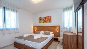 A modern bedroom with a wooden bed, a bedside table, a mirror, and a colorful abstract painting on the wall. - Holiday apartment with shared-use pool (Sv. Filip i Jakov)