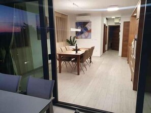 A modern dining area with a wooden table and chairs, a potted plant, and a view through a glass door. - Holiday apartment with pool and air conditioning (Sv. Filip i Jakov)