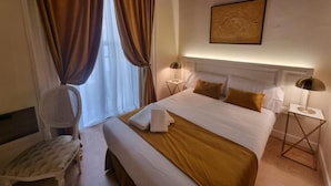 A hotel room with a large bed, a bedside table with a lamp, a chair, and a window with curtains. - Le Petit Palu Flora (Madrid)