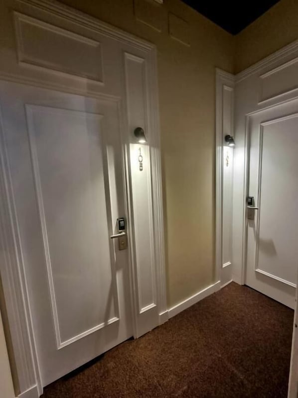 A hallway with three white doors, each with a doorbell and a light above the door. - Le Petit Palu Flora (Madrid)