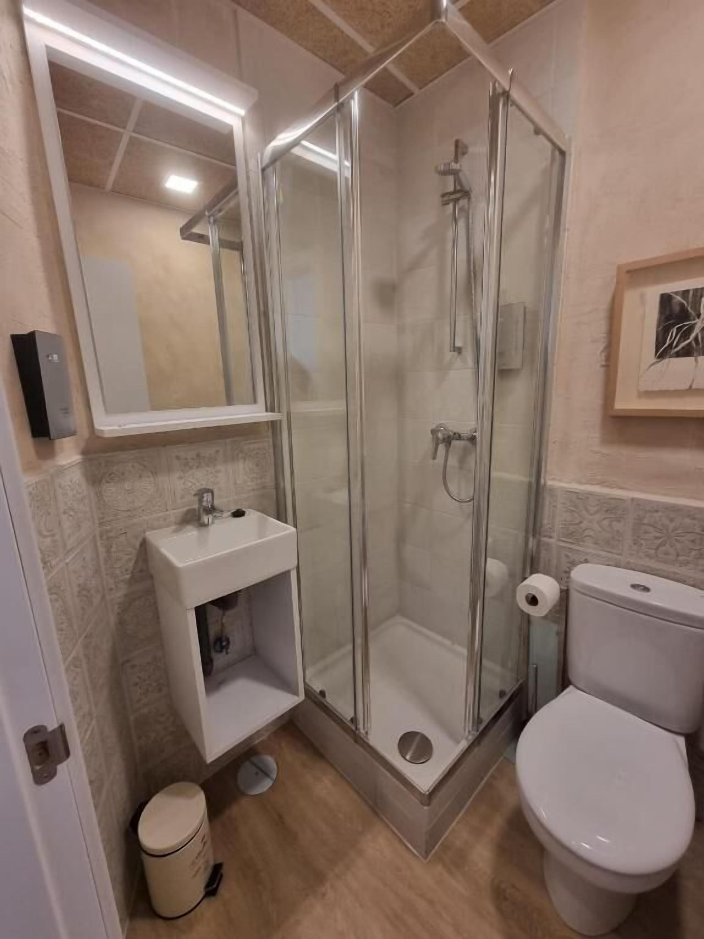 Un baño moderno con ducha envuelta en vidrio, un lavabo blanco con espejo y un inodoro.