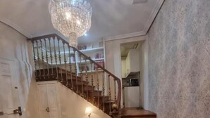 A grand staircase with a chandelier, wooden flooring, and a view into a kitchen area. - Le Petit Palu Flora (Madrid)