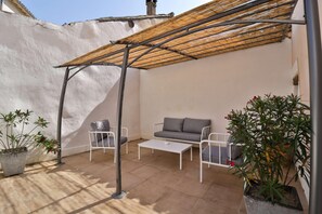 A patio area with a white metal table, two chairs, a grey sofa, and potted plants. - Château De Mazan - Handwritten Collection (Mazan)