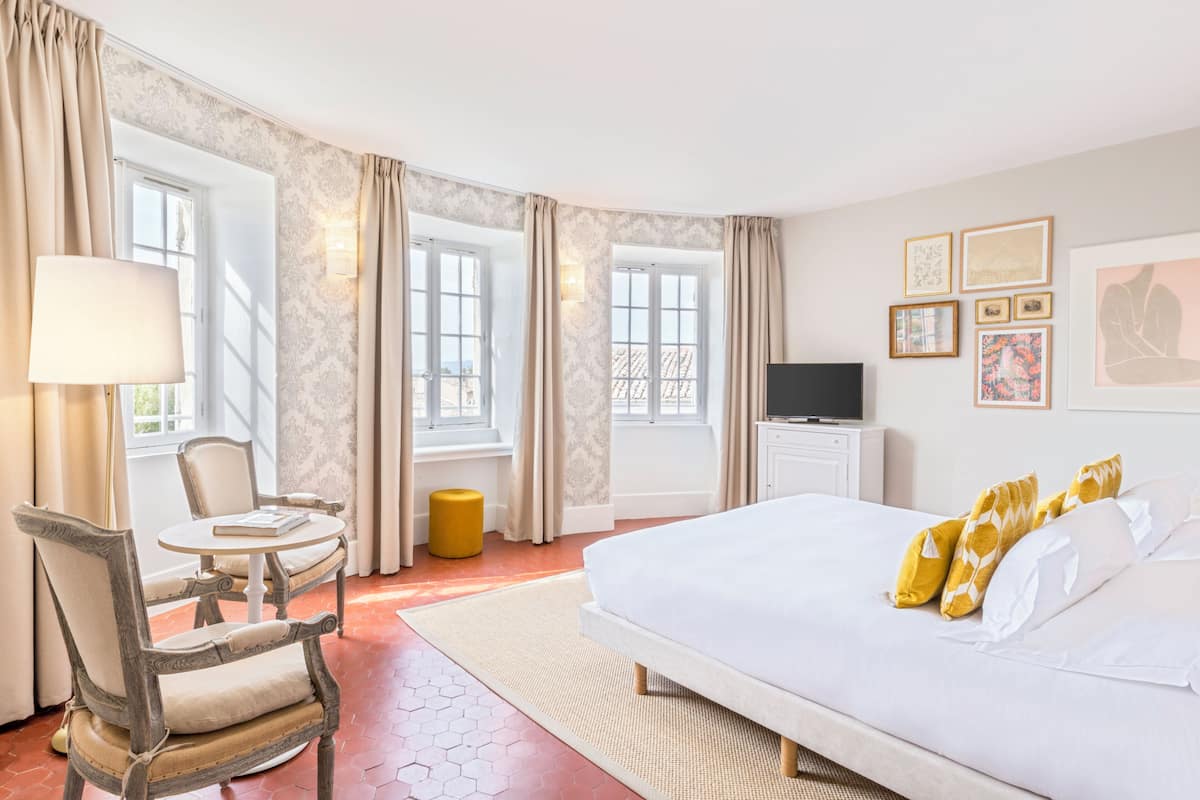A hotel room with a bed, a chair, a table, a lamp, and a TV.