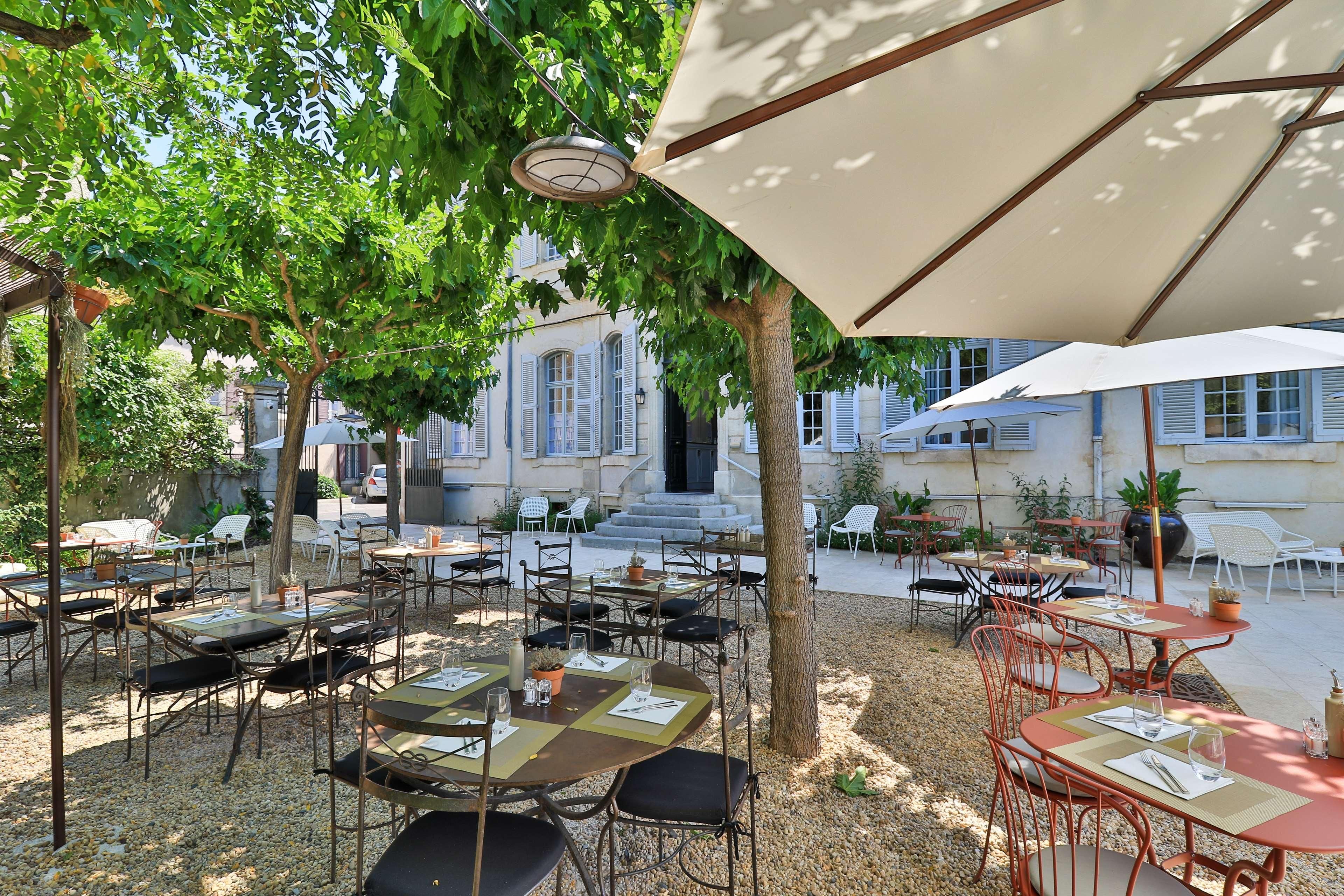 An outdoor café with tables and chairs, surrounded by trees and buildings.