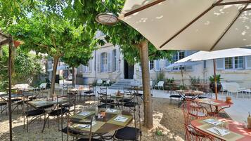 An outdoor café with tables and chairs, surrounded by trees and buildings.