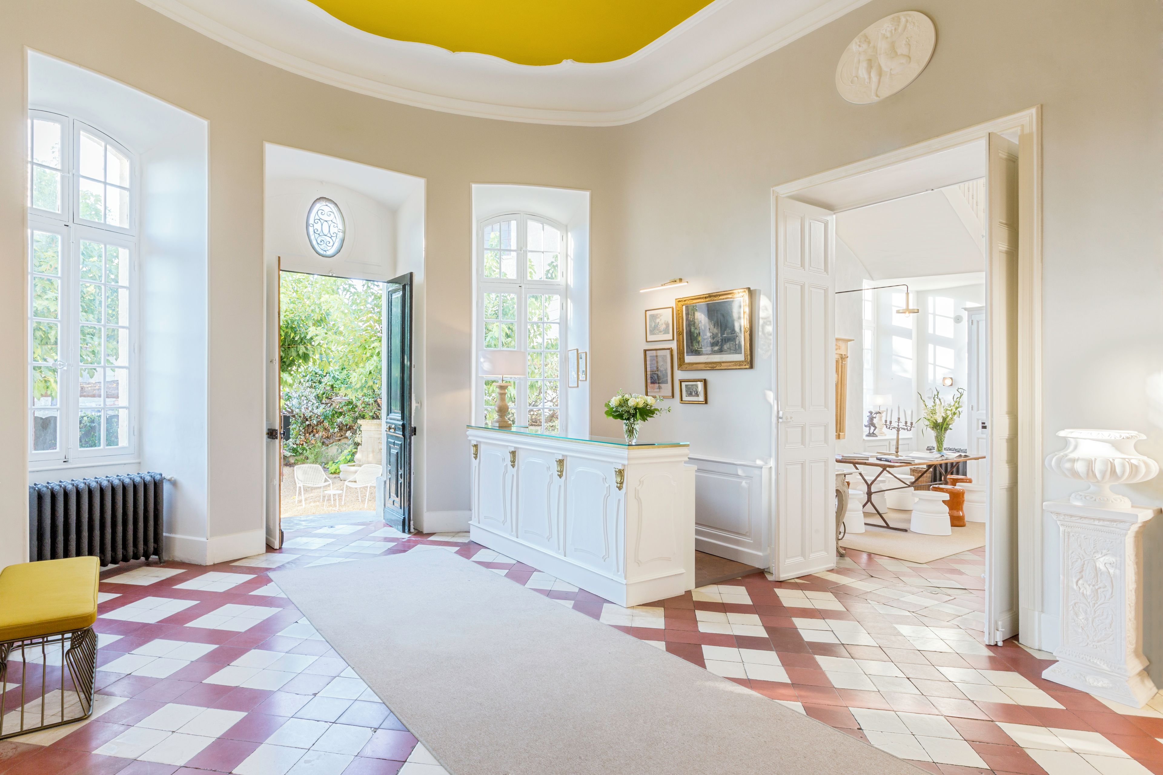 A hallway with a patterned floor, a white console table with a vase, and a door leading to a room with a table and chairs.