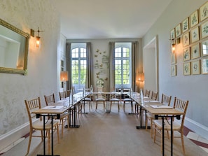 Ein Esszimmer mit einem langen Tisch, StĂŒhlen und groĂen Fenstern mit VorhĂ€ngen.