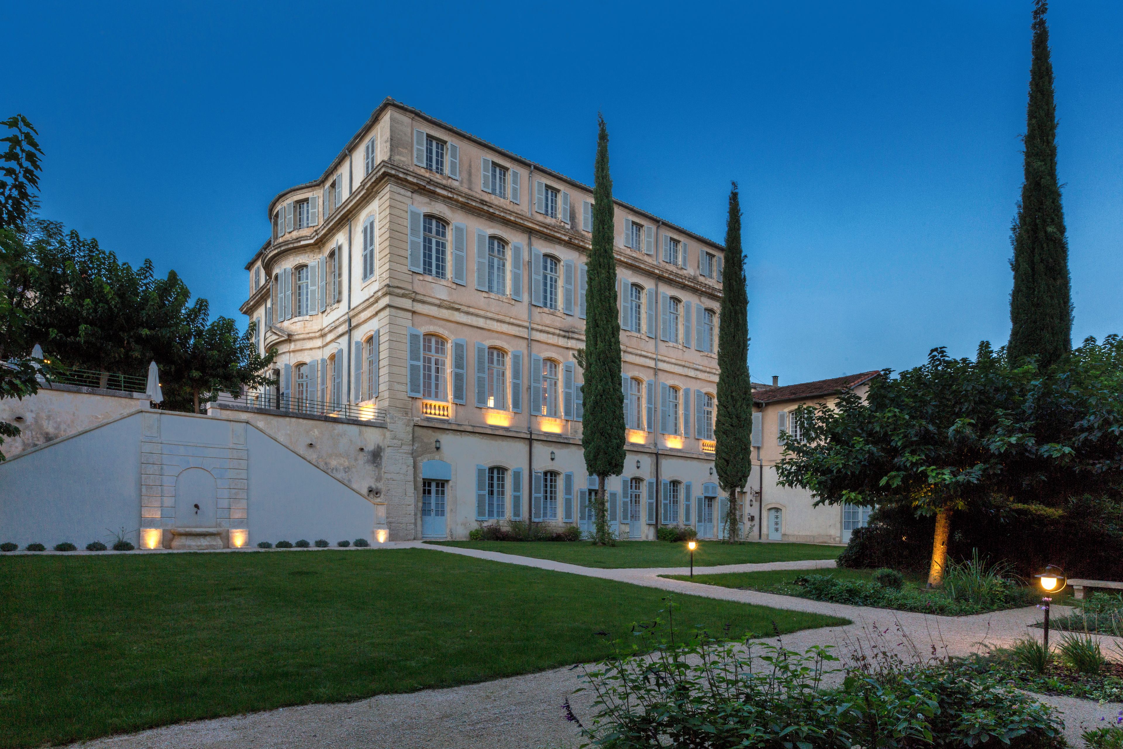A large, multi-story building with a symmetrical facade, a central staircase, and a well-maintained garden with pathways.