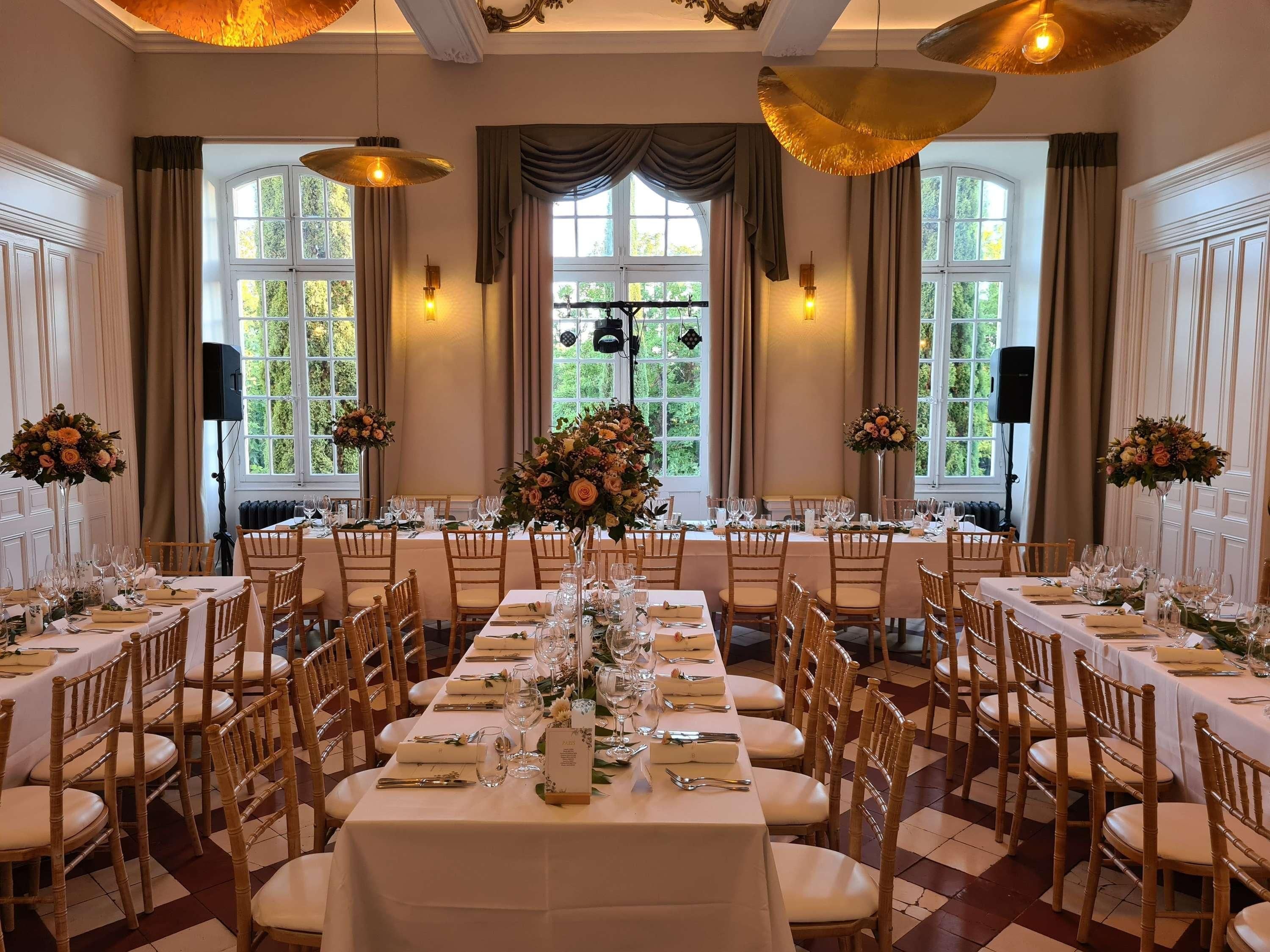 Un comedor formal con mesas largas, sillas de madera y centros de mesa con flores.