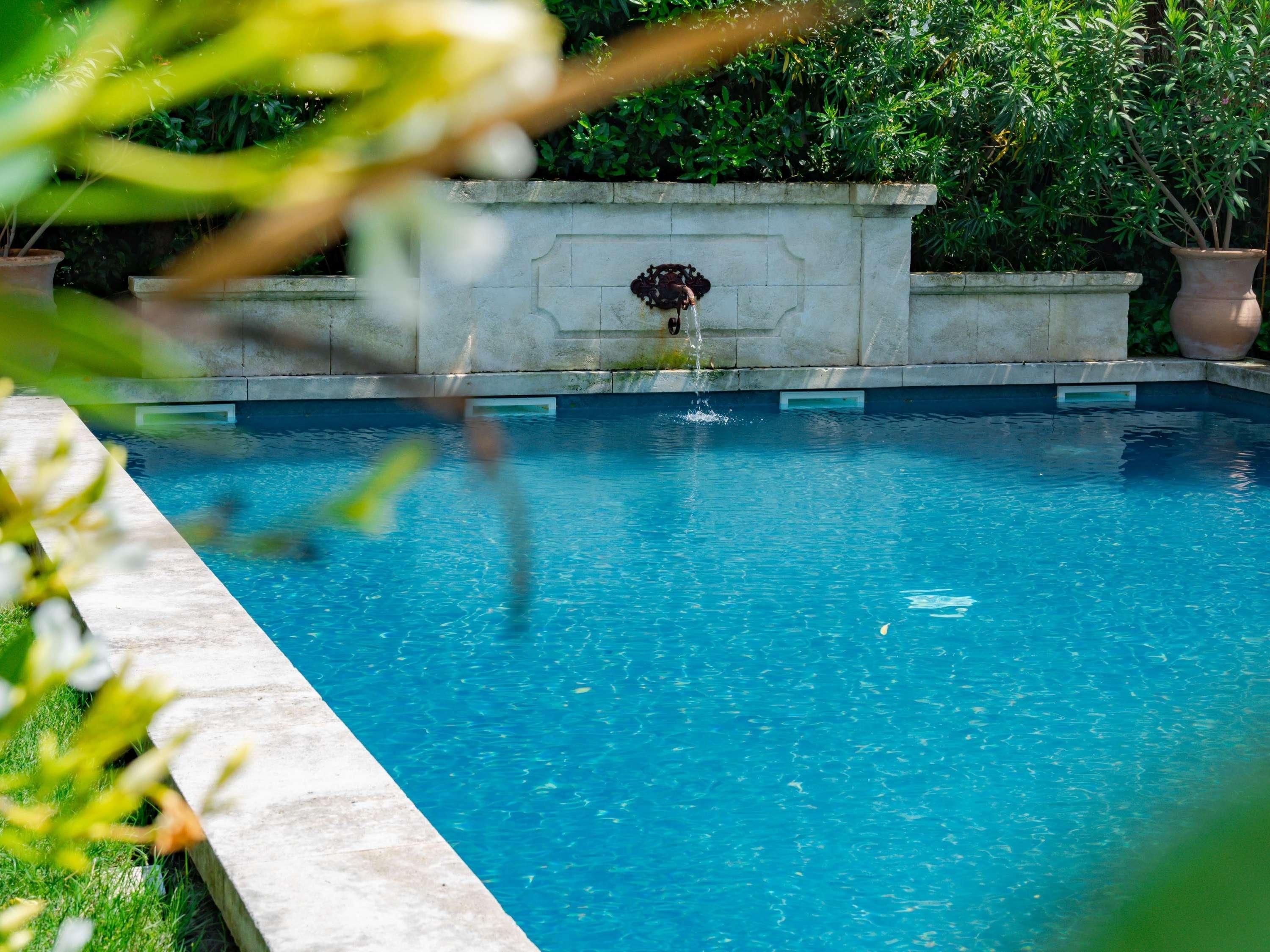A swimming pool with a stone wall, surrounded by greenery.