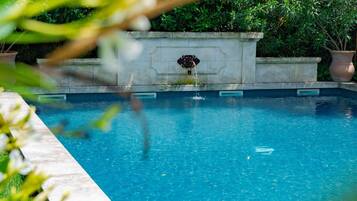 A swimming pool with a stone wall, surrounded by greenery.