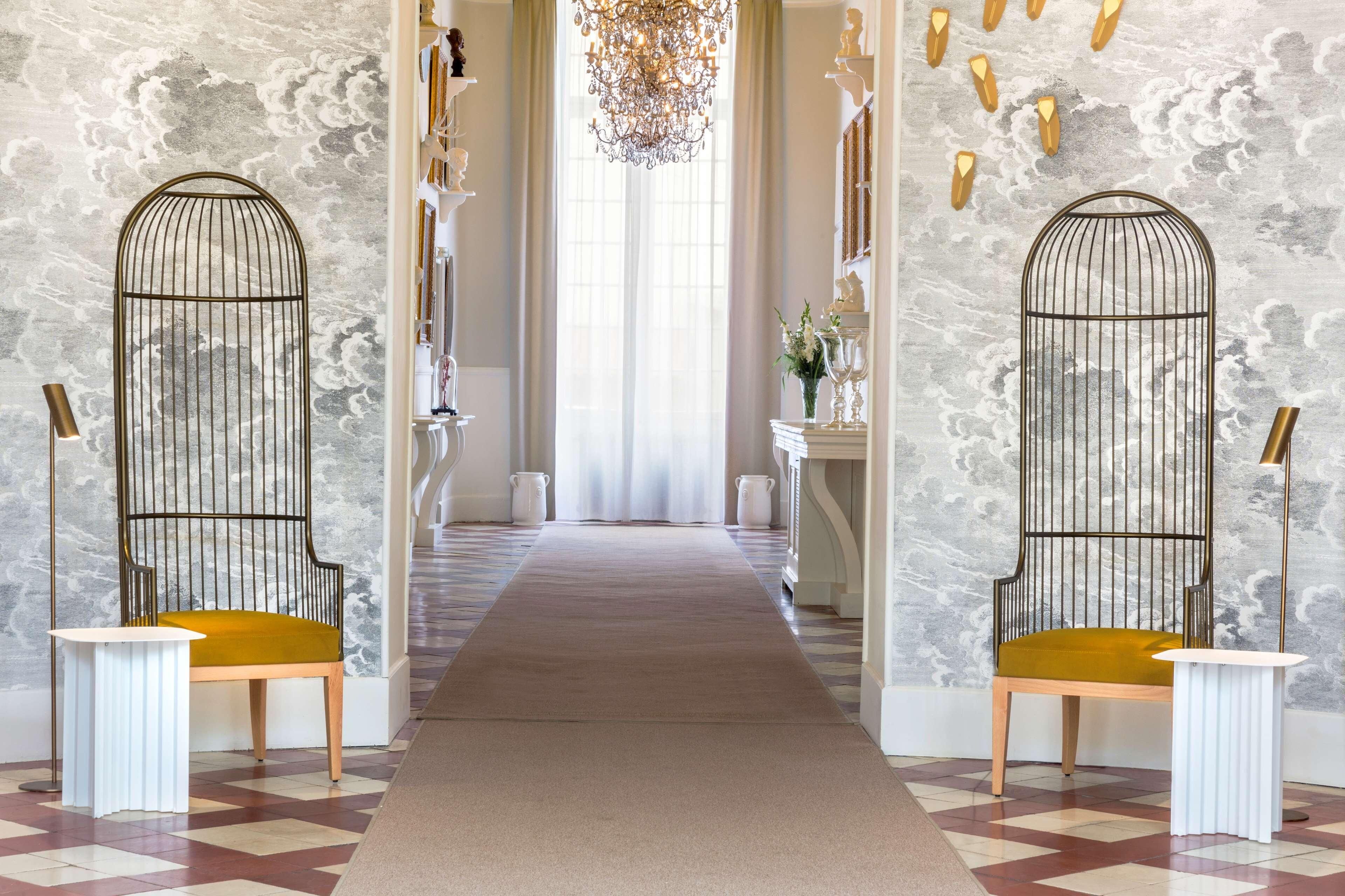 Un pasillo con piso estampado, un sendero central alfombrado y dos sillones ornamentados con mesas blancas.