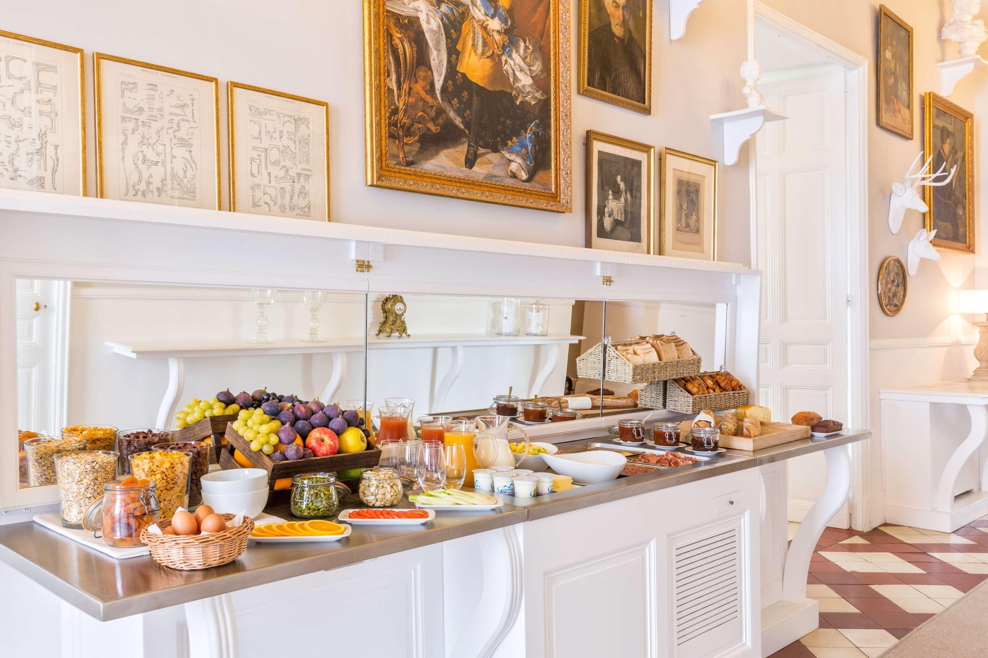 Un bufé de desayuno con diversos alimentos y bebidas, obras de arte enmarcadas en las paredes, y una decoración interior en tonos blancos.