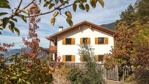A two-story house with a balcony, surrounded by trees and a mountain view. - Apartment 'Pföslhof Weinberg' with Mountain View, Shared Garden and Wi-Fi (Leifers)