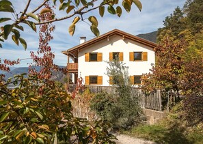 Une maison à deux étages avec un balcon, entourée d’arbres et offrant une vue sur la montagne.