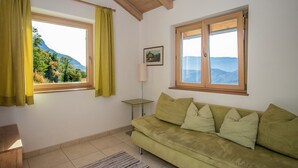 A room with a green sofa, two windows with curtains, a picture on the wall, and a small table. - Apartment 'Pföslhof Weinberg' with Mountain View, Shared Garden and Wi-Fi (Leifers)