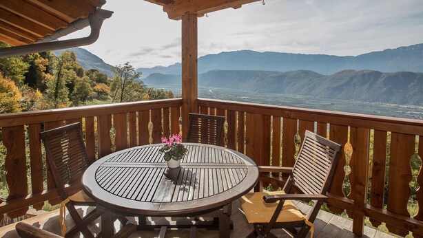 A wooden deck with a round table and chairs, a potted plant, and a view of distant mountains. - Apartment 'Pföslhof Weinberg' with Mountain View, Shared Garden and Wi-Fi (Leifers)